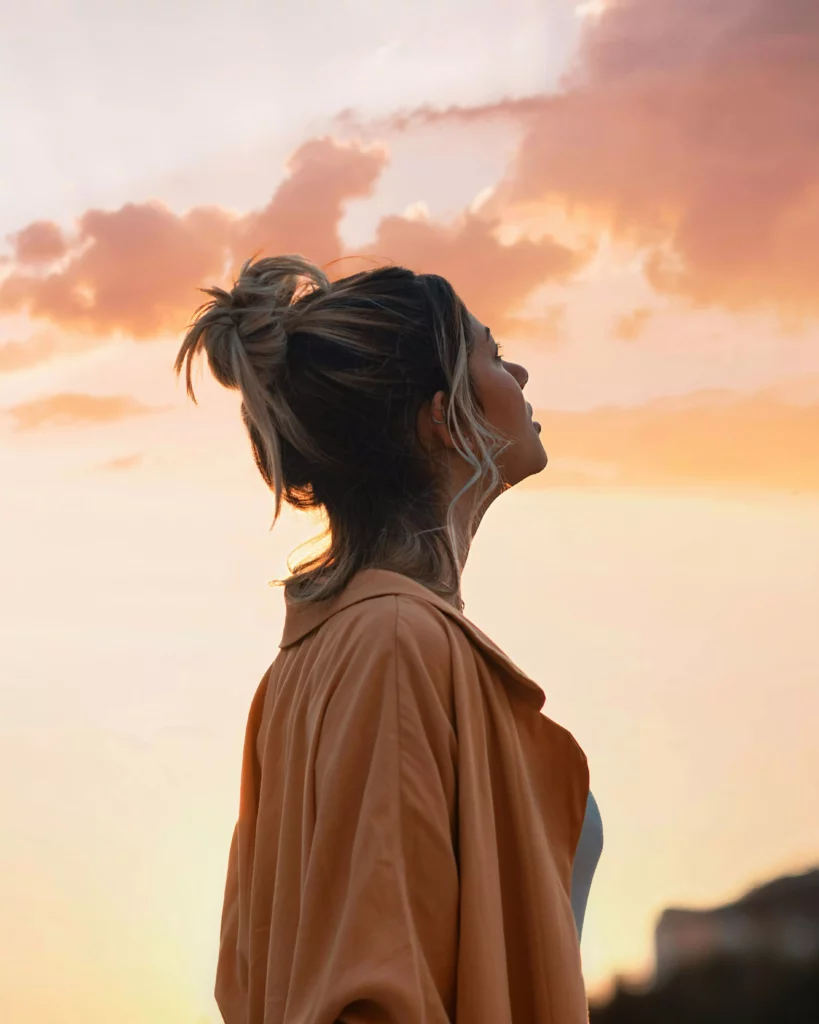 Une femme lève la tête vers le ciel avec espoir. Recherche intérieure, épanouissement personnel, sens de vie, éveil de conscience.
